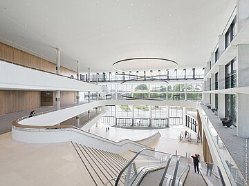 „Weitläufige Eingangshalle des CCH mit modernen Treppen, Glasfronten und einer großen runden Deckenleuchte.“